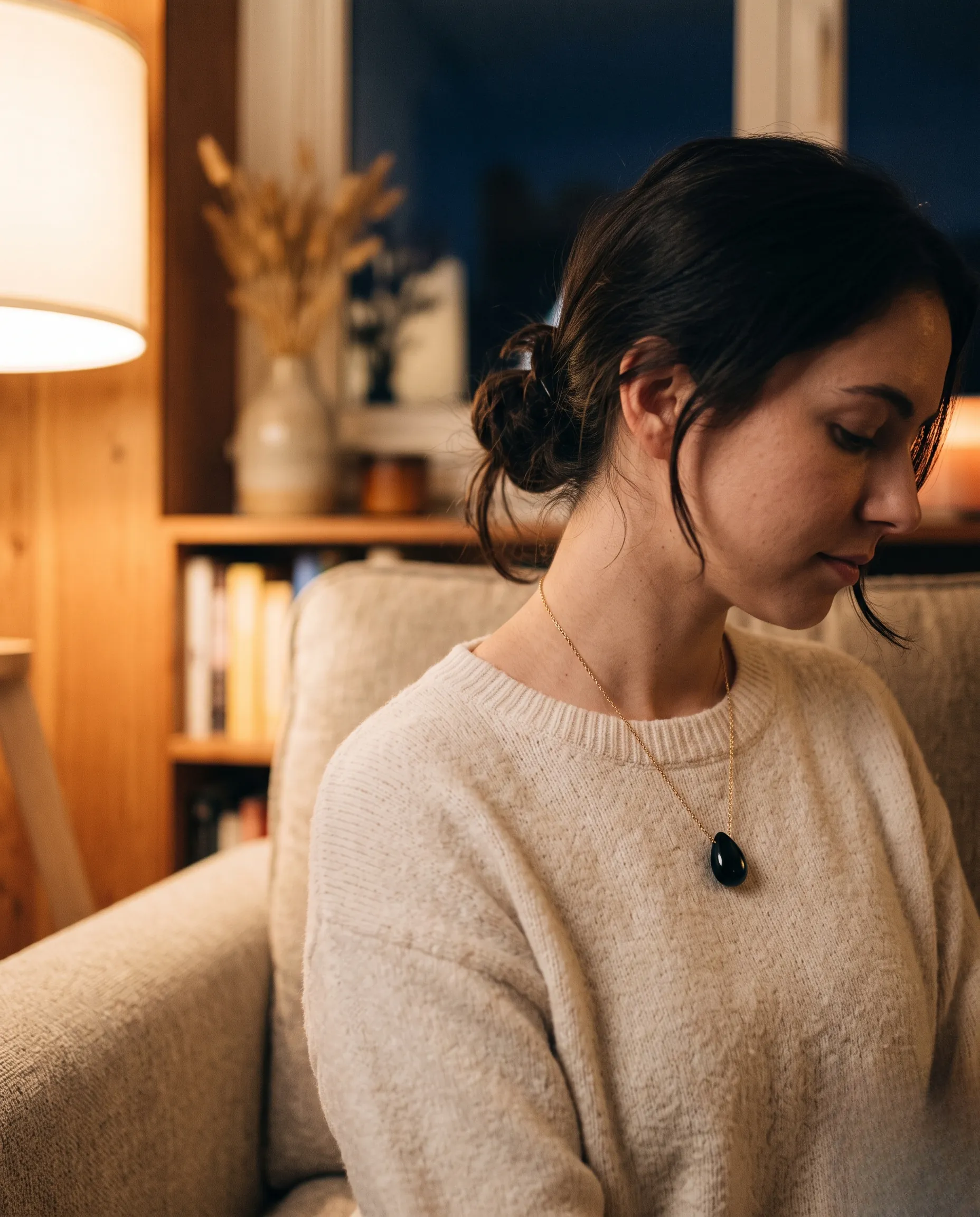 Collier délicat avec un pendentif en obsidienne noire porté par une personne dans une lumière douce.