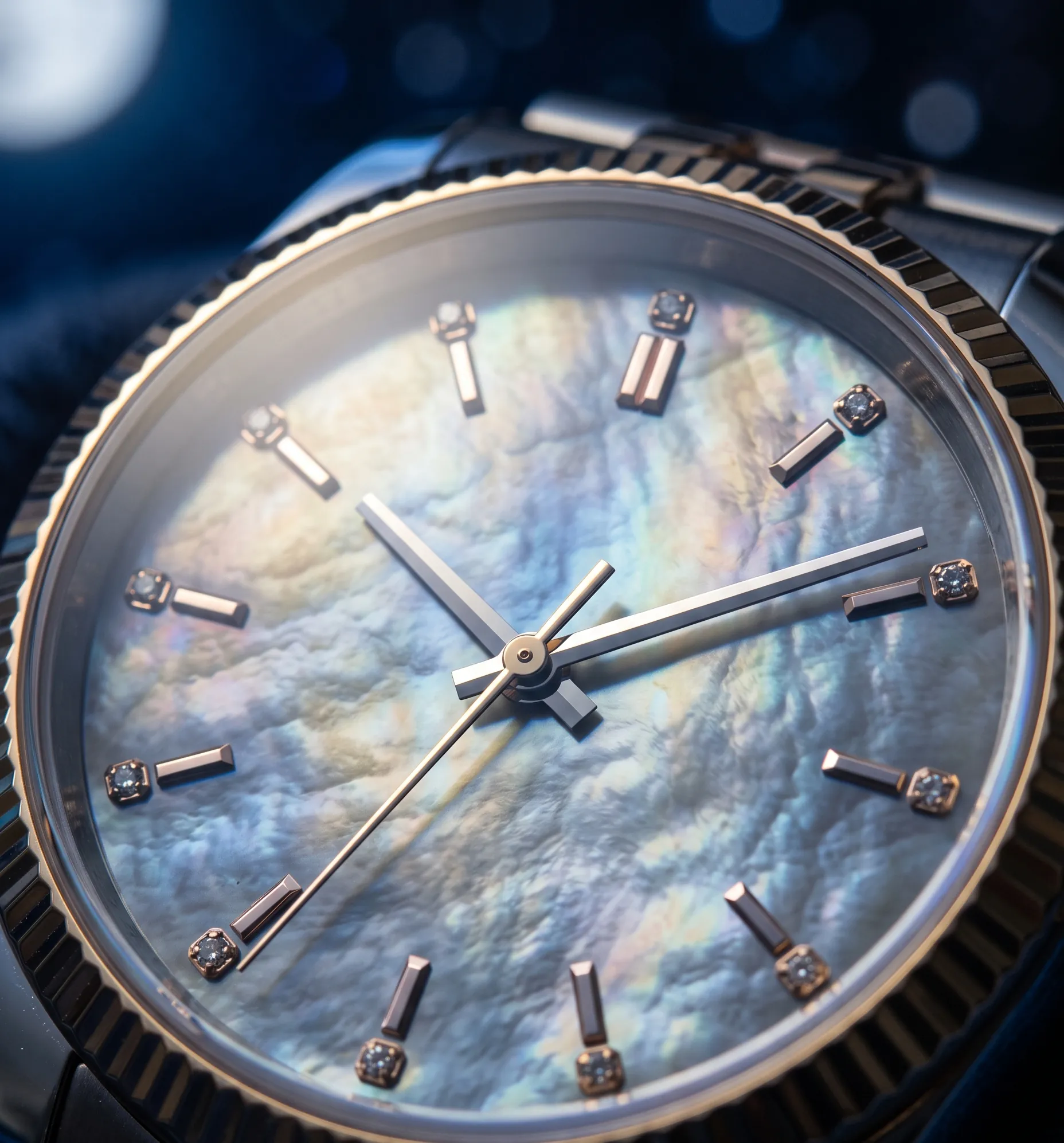 Gros plan macro sur un cadran de montre en nacre naturelle aux reflets changeants et lunaires.