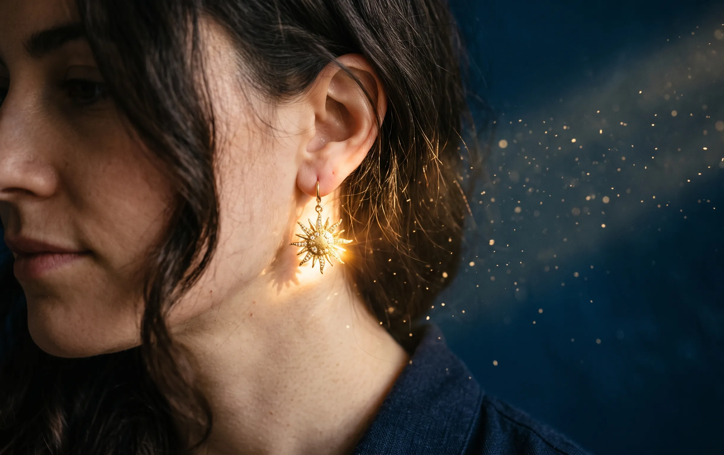 Gros plan sur une boucle d'oreille soleil en métal précieux capturant un rayon de lumière chaleureux.